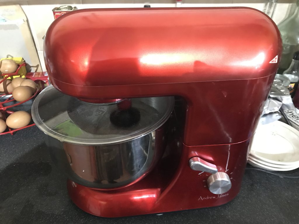Shiny red stand mixer with syrup being whisked.