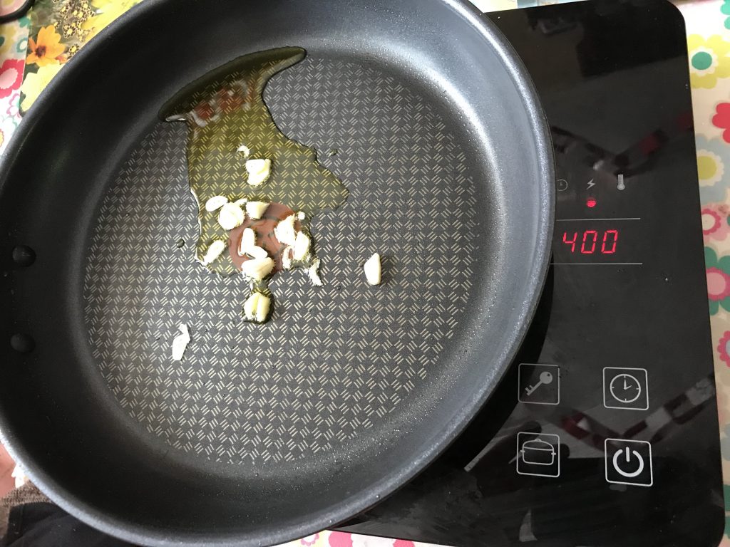 A fryig pan on an induction hob with olive oil and garlic