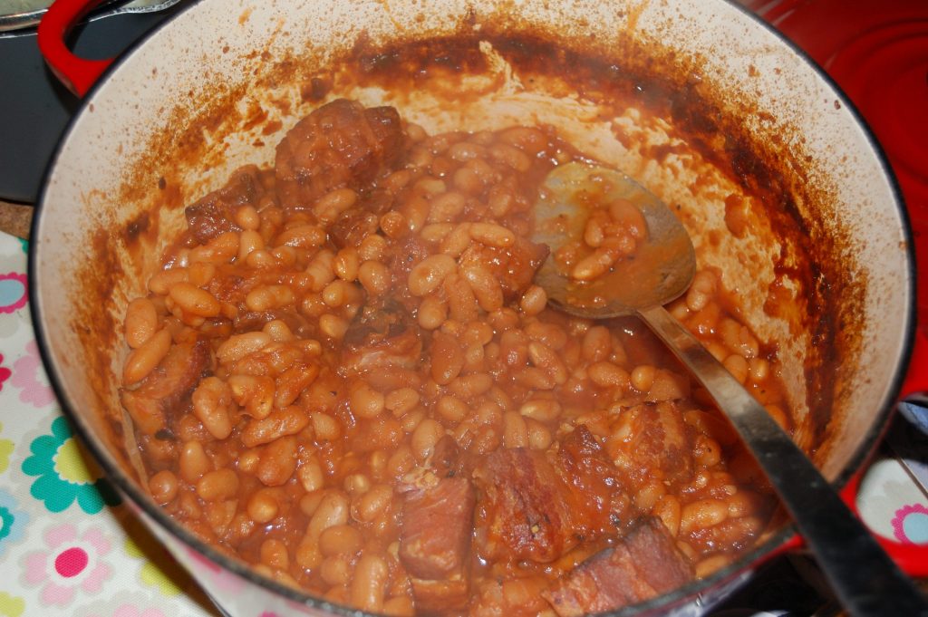 A pan with cooked homemade baked beans part way through serving