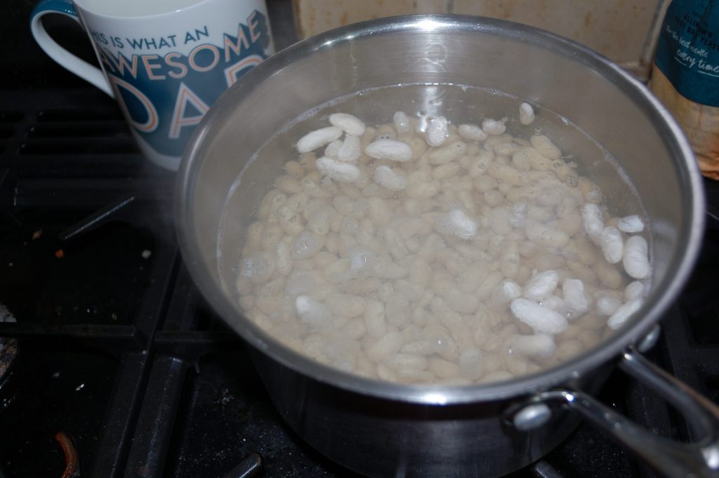 A steel pan with some soaked cannellini beans being brought to the simmer.