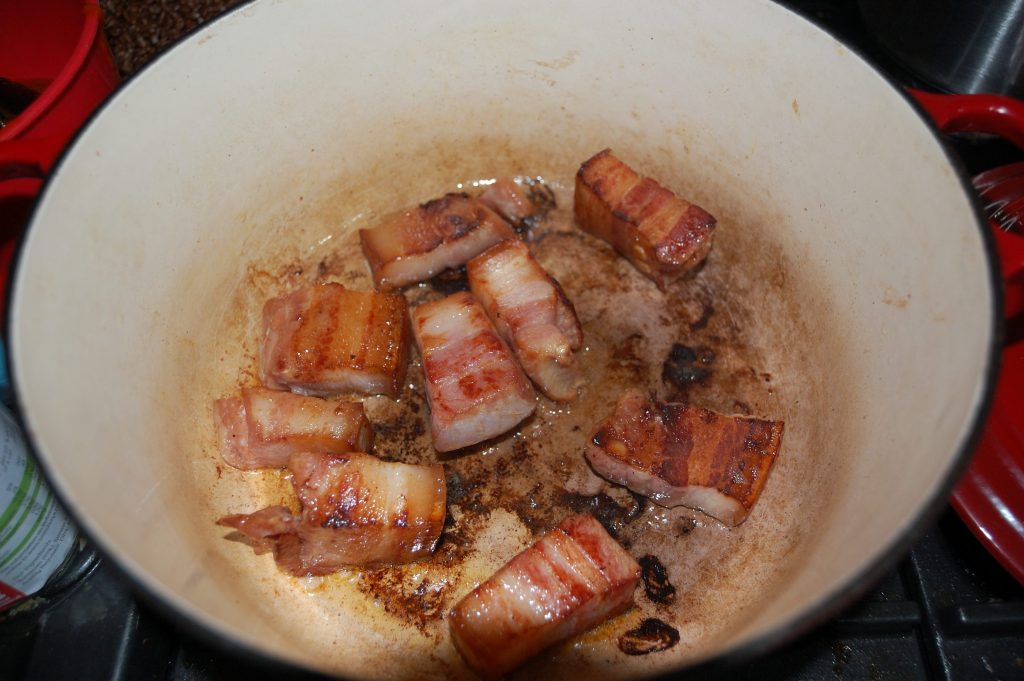 An enameled pan with some nicely browned bacon chunks.
