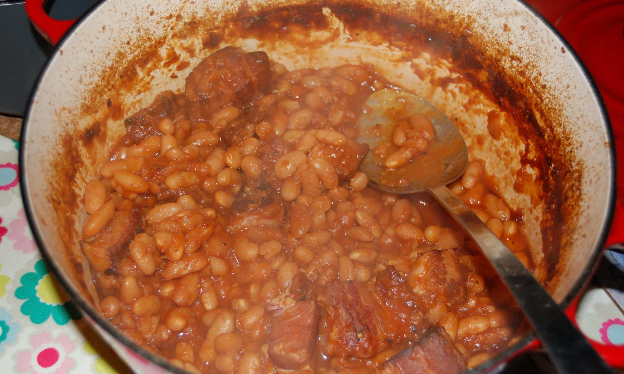A pan with cooked homemade baked beans part way through serving
