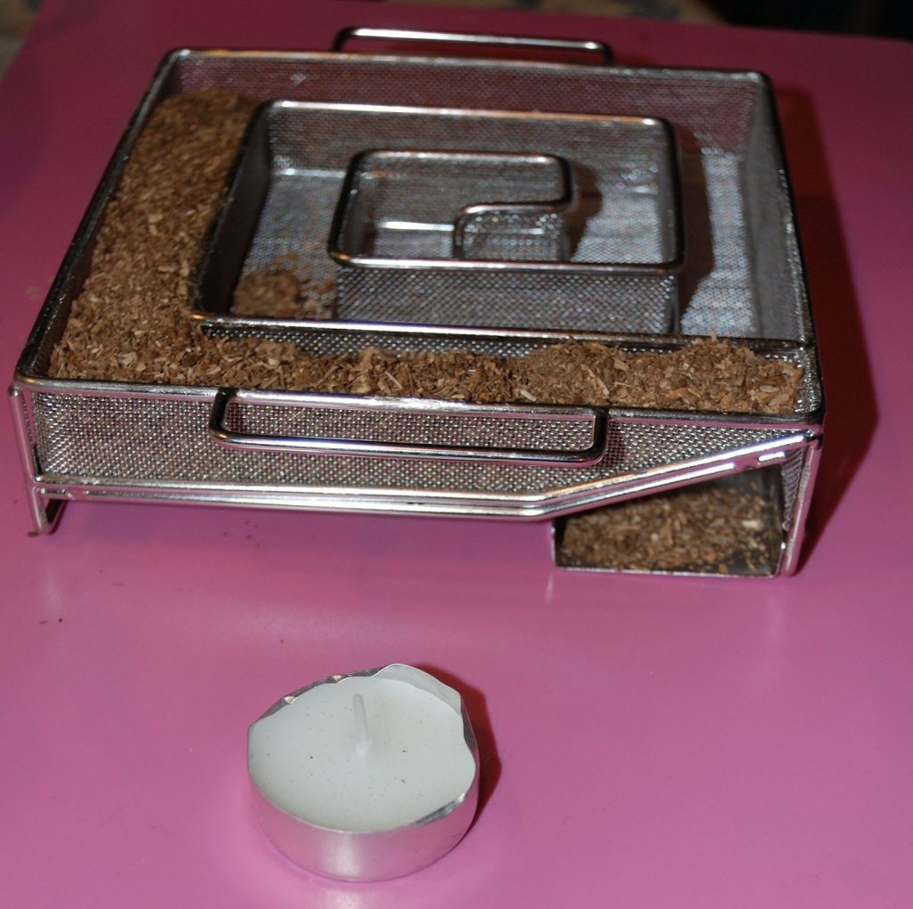 A stainless steel ProQ cold smoke generator quarter filled with oak dust.