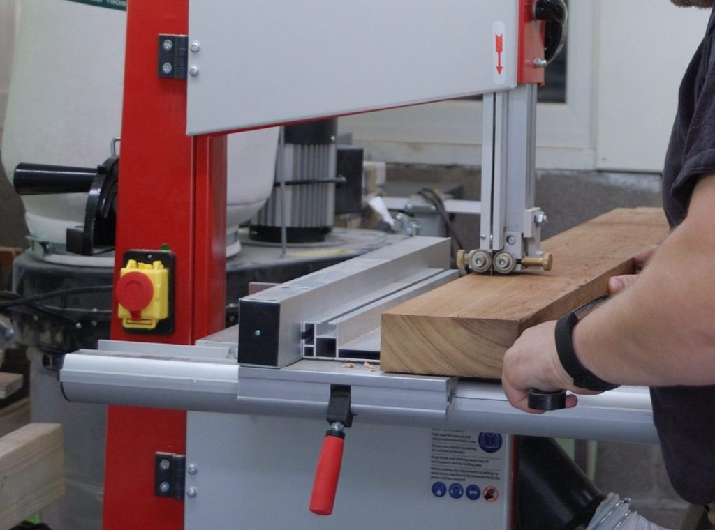 GymCee using a bandsaw to rip down sme wood.