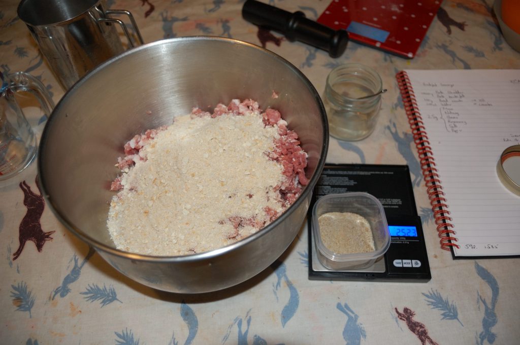 A picture of a mixing bowl with minced pork, breadcrumbs and a scale with sausage seasoning.