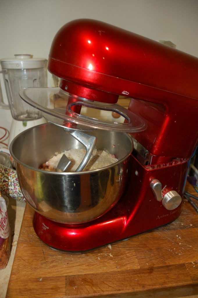 A red stand mixer with sausage ingredients waiting to be mixed.