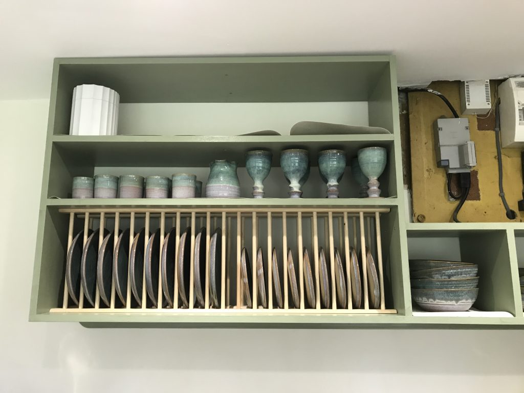 A green wall cupboard with plate rack.