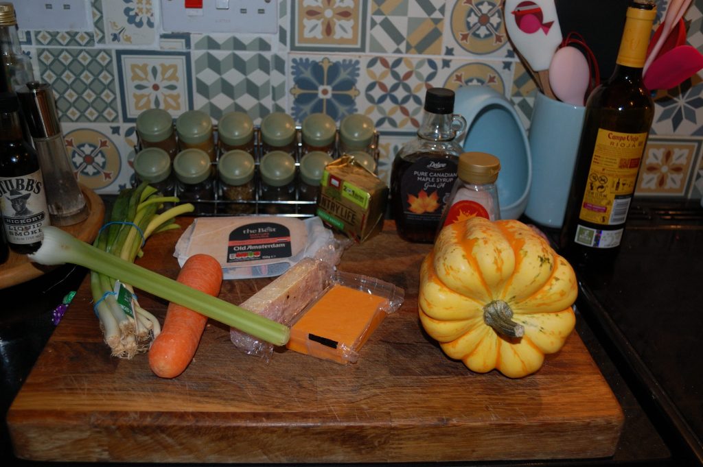 A chopping board with pupkin, carrot, celery, cheese, maple syrup and more.