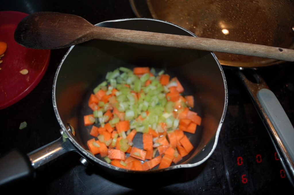 An out of focus photo of a small pan with carrots, celery and spring onion.