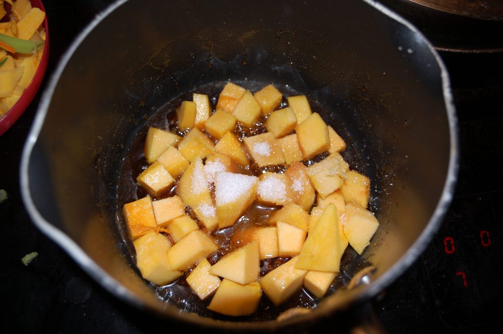 A small pan with diced raw pumpkin and sugar and maple syrup.